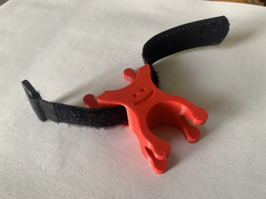 3D Printed bike pump bracket. Red. Smiley face, happy! Velcro strap through the middle. 