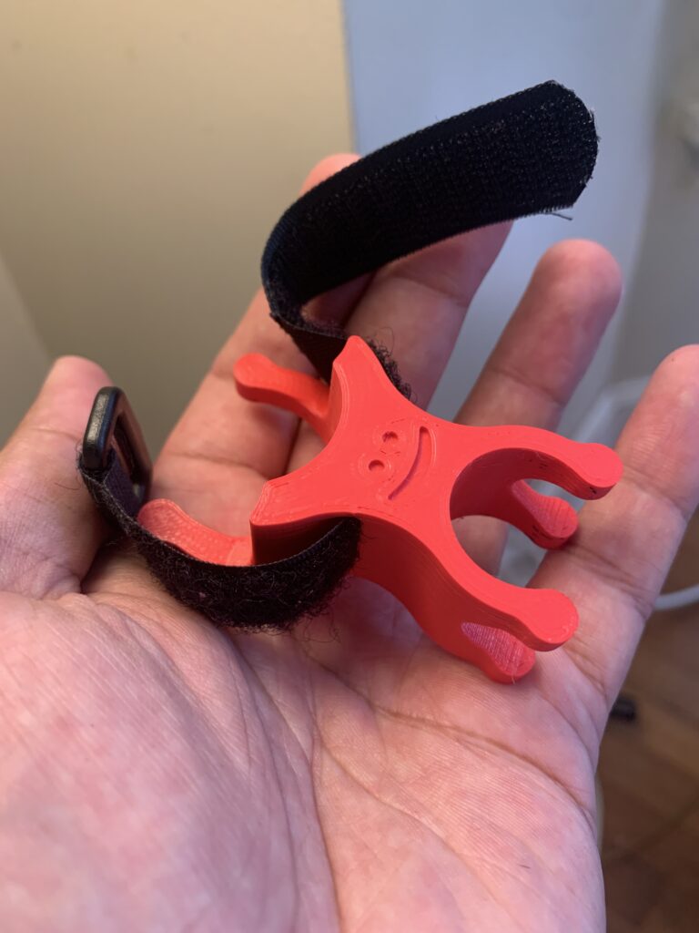 3D Printed bike pump bracket. Red. Smiley face, happy! Velcro strap through the middle. 